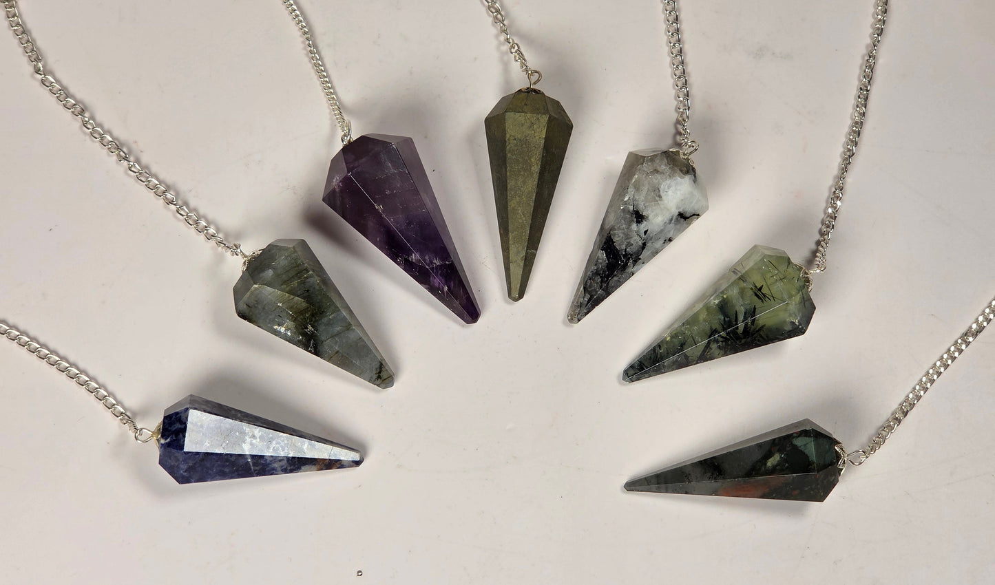Six silver cone pendants made from different polished crystals, arranged in a circle on a light off-white background.