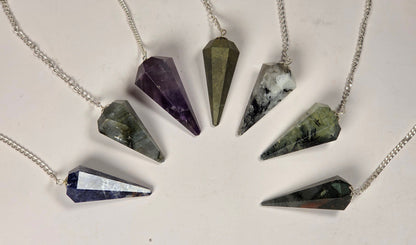 Six silver cone pendants made from different polished crystals, arranged in a circle on a light off-white background.