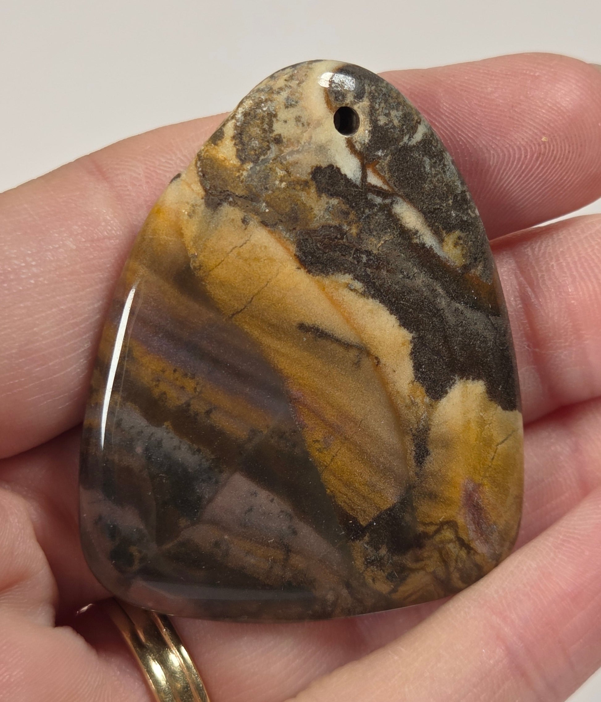 A polished, hand-shaped stone pendant with a natural tiger's eye pattern in shades of brown, yellow, and black, held in a person's hand.