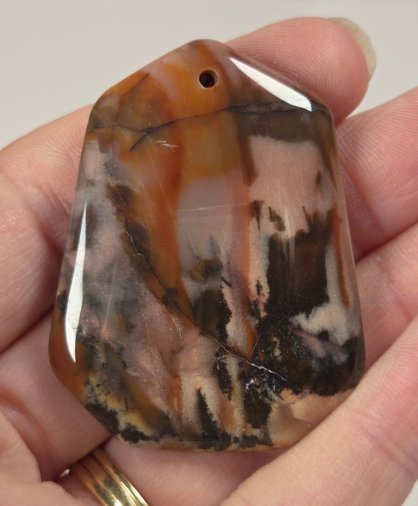 A polished stone pendant with a natural marbled pattern of brown, black, and cream, held in a person's hand.