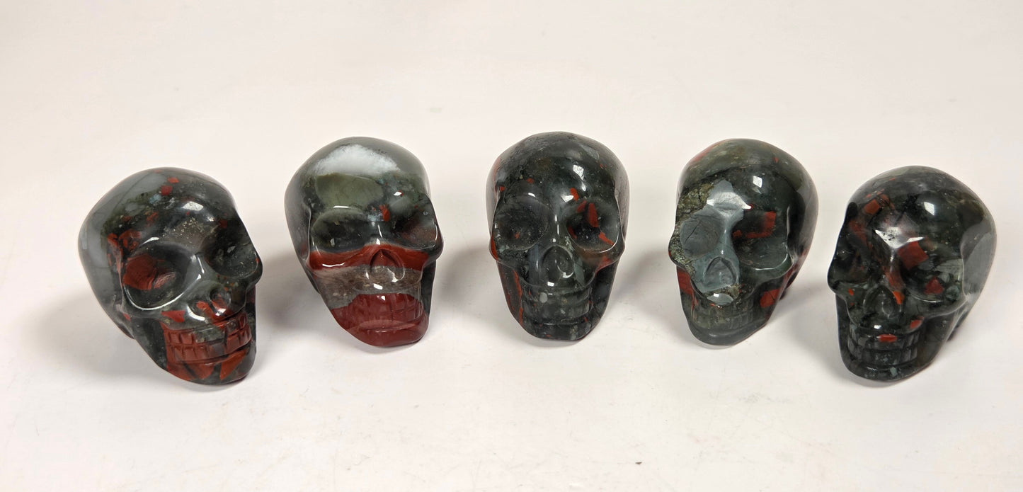 Five polished red jasper skull figurines lined up on a white marble surface against a white marble background.
