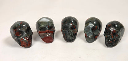 Five polished red jasper skull figurines lined up on a white marble surface against a white marble background.