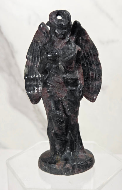 A dark stone angel statue with outstretched wings and a halo, displayed on a clear acrylic stand against a light marble-patterned background.