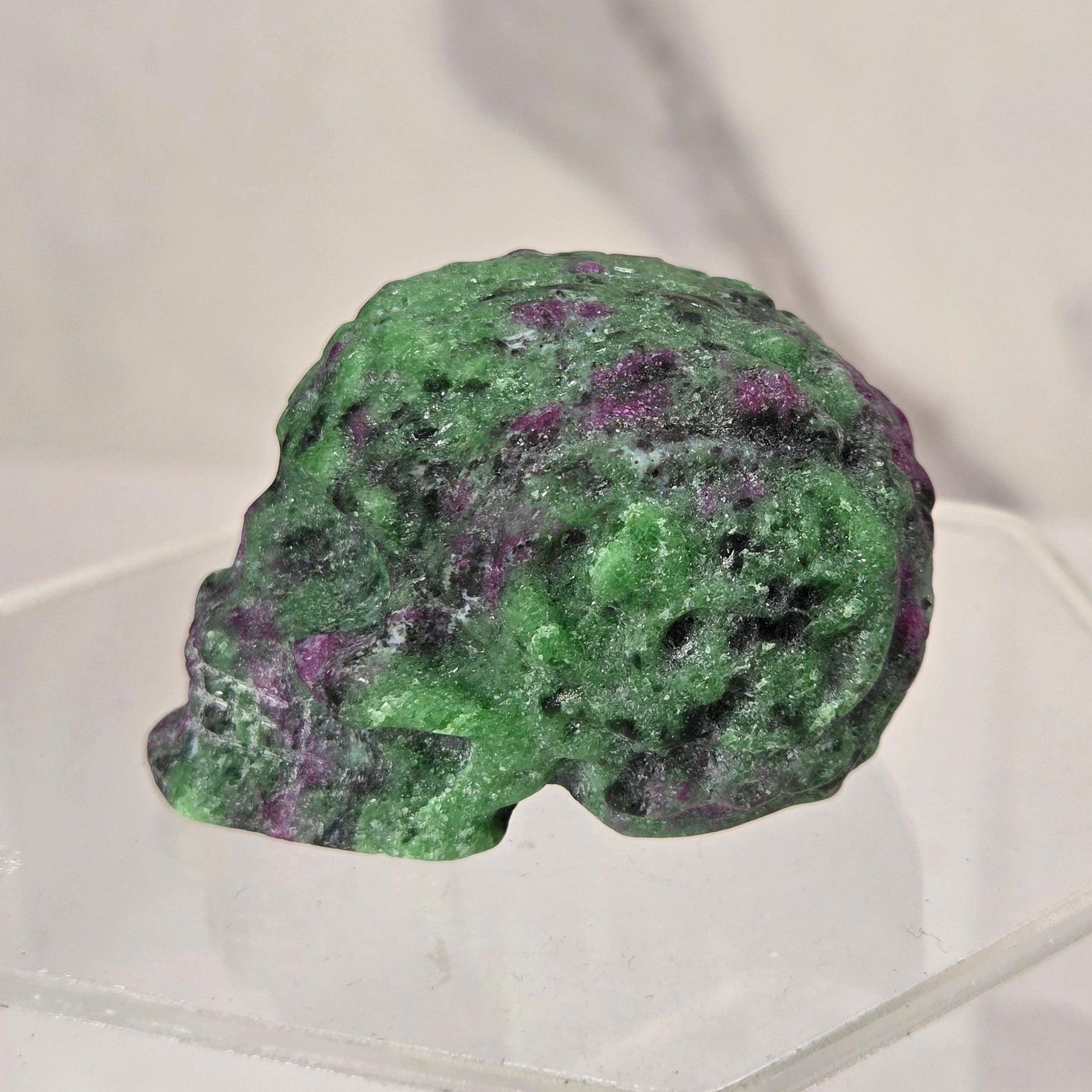 A green and purple marbled decorative stone sculpture displayed on a clear acrylic stand against a light marble-patterned background.