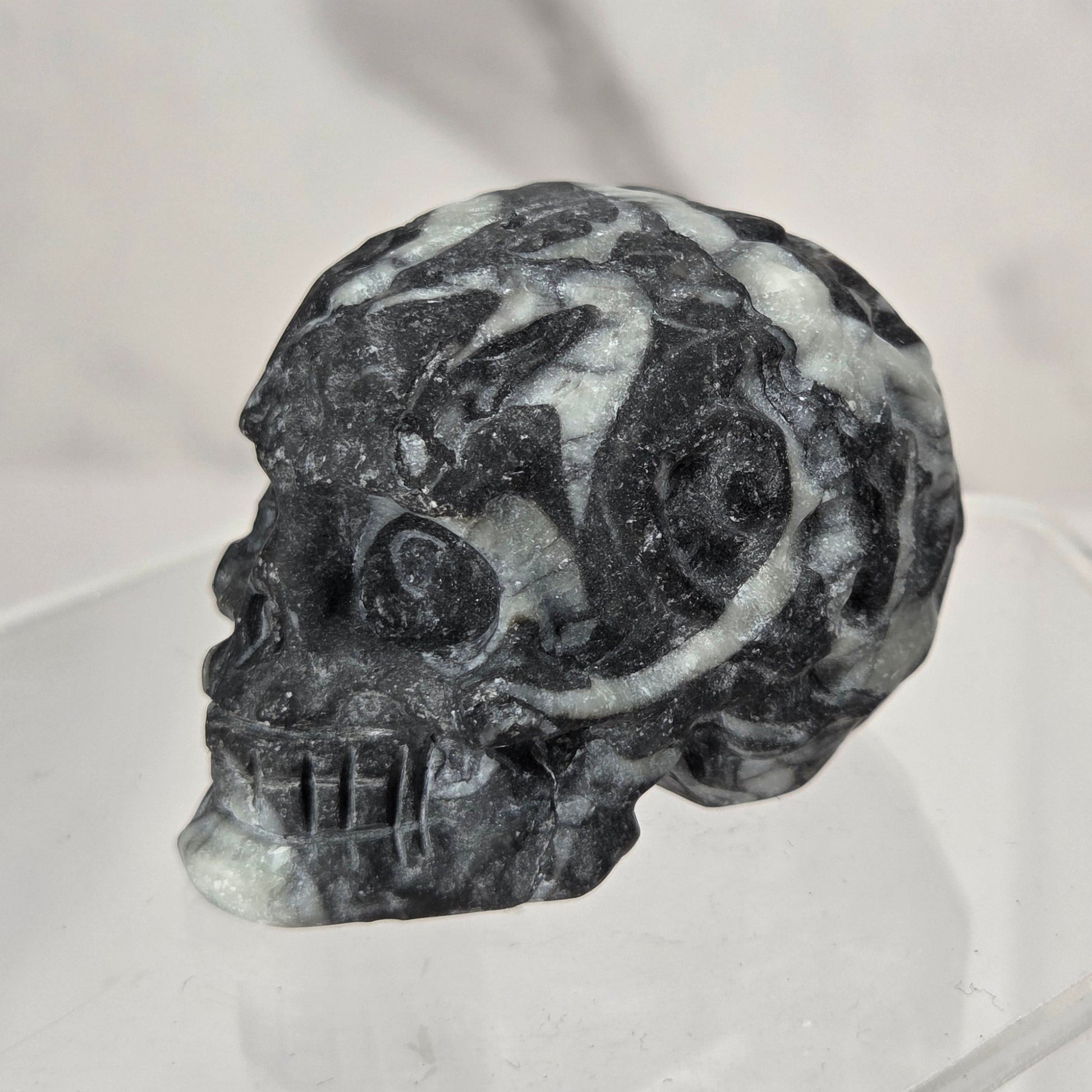 A carved black and white marbled skull displayed on a clear acrylic stand against a light gray marble-patterned background.