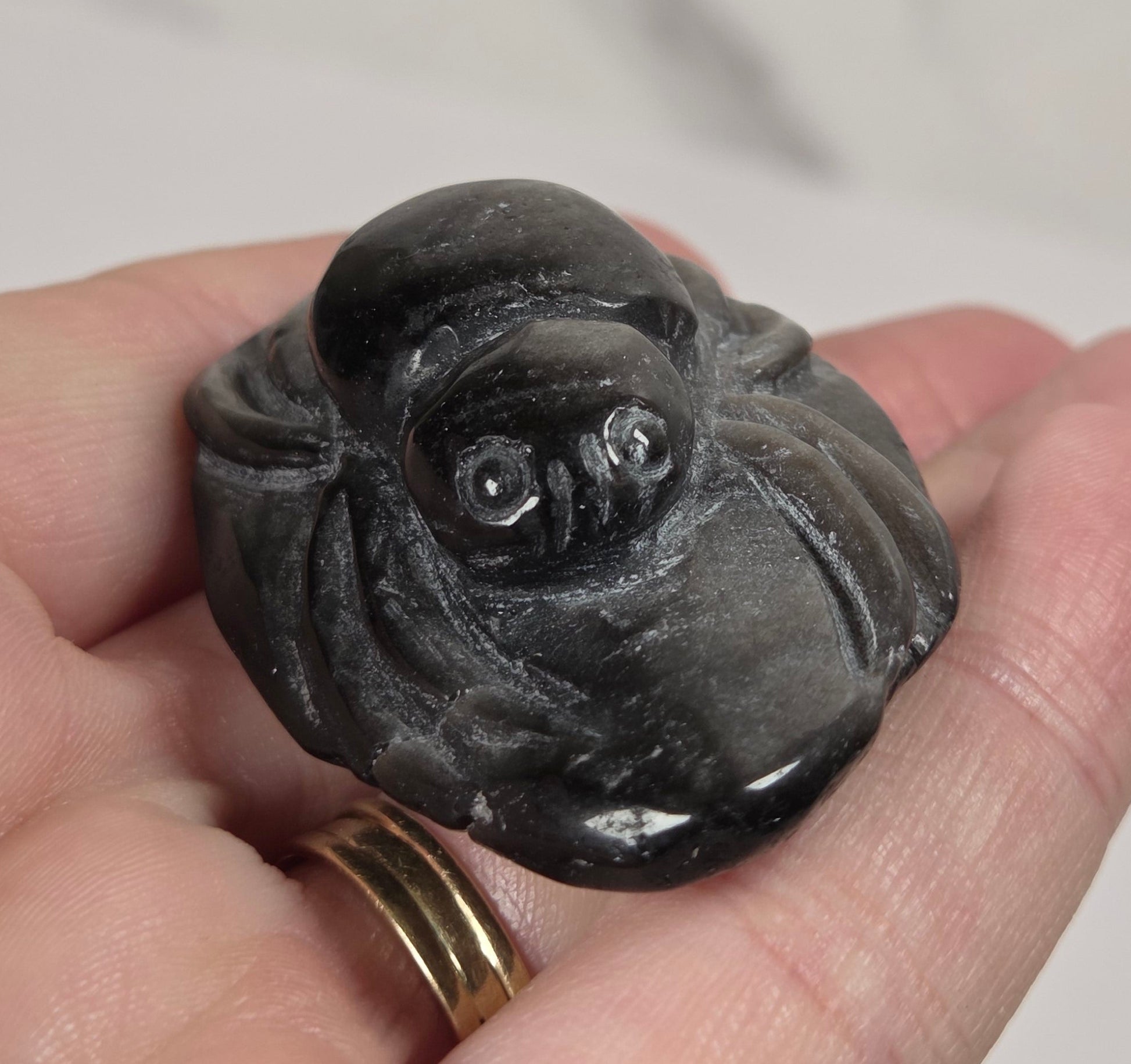 A hand holding a small carved dark stone figurine with a glossy finish, set against a light gray marble-patterned background.