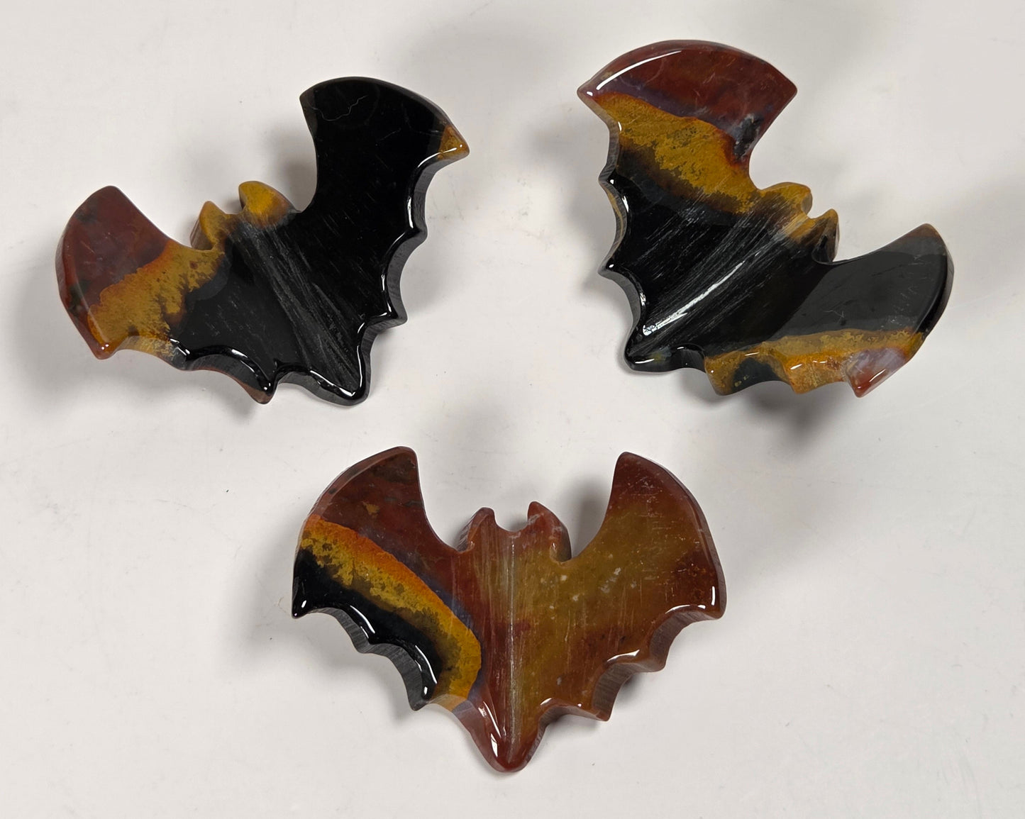 Three sea jasper 3D bat carvings with black, red and tan coloring on a white background