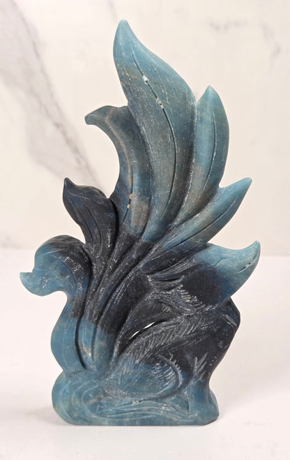 Crystal carving of a 9 tail fox made of trolleite with blue and black coloring on a white background
