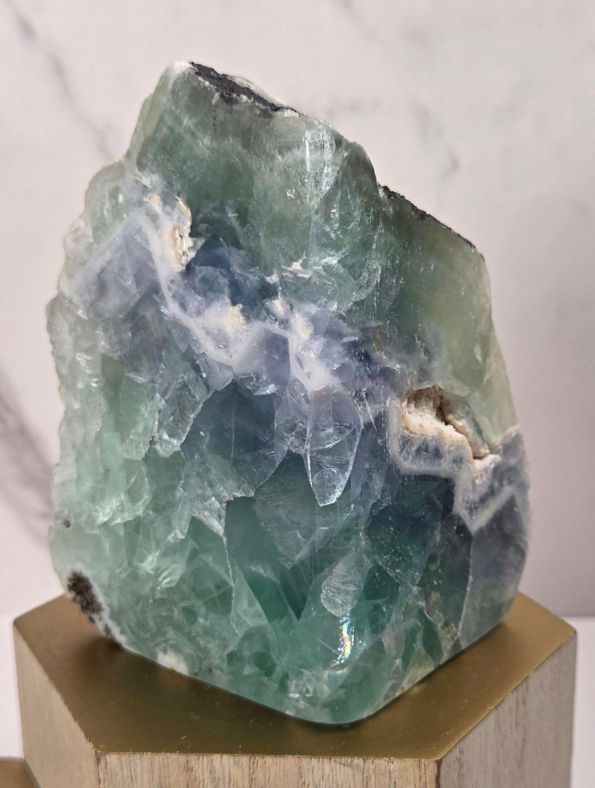 raw mineral and geode specimens displayed on wooden blocks against a white marble-patterned background. The stones feature natural patterns in shades of green, purple, blue, and gray.