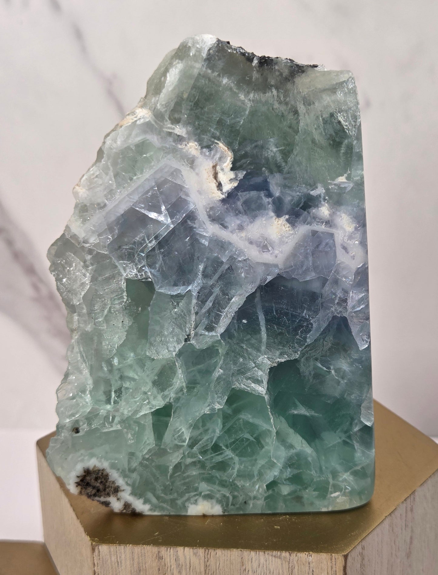 raw mineral and geode specimens displayed on wooden blocks against a white marble-patterned background. The stones feature natural patterns in shades of green, purple, blue, and gray.