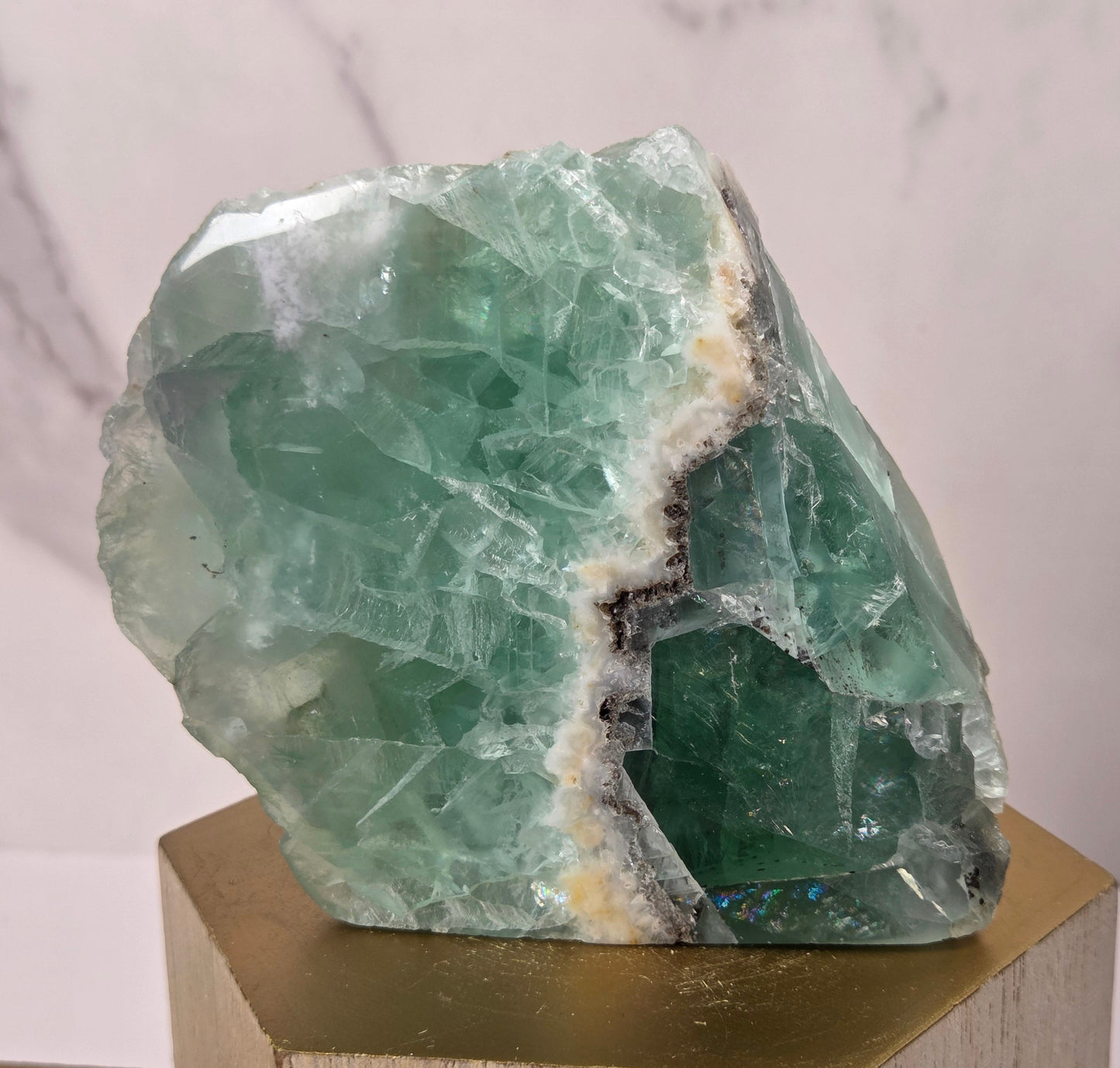 raw mineral and geode specimens displayed on wooden blocks against a white marble-patterned background. The stones feature natural patterns in shades of green, purple, blue, and gray.