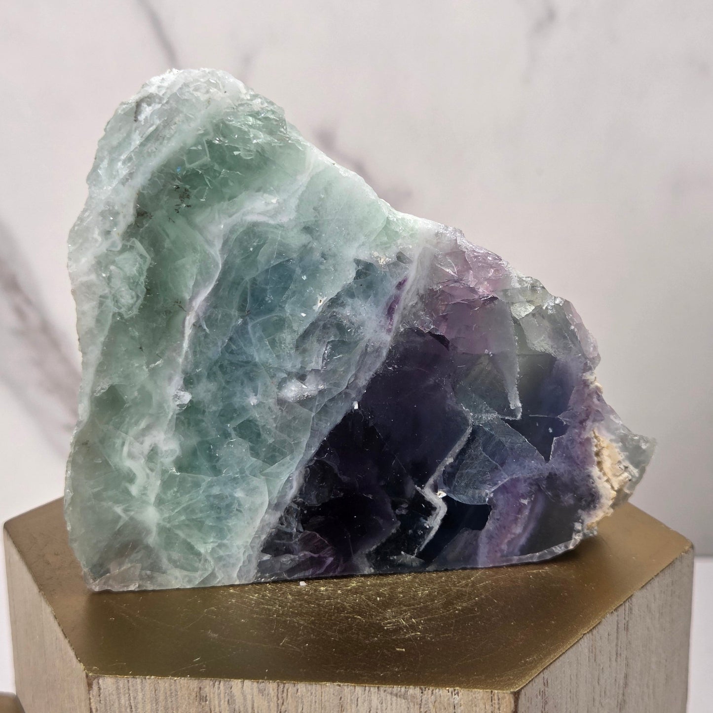 raw mineral and geode specimens displayed on wooden blocks against a white marble-patterned background. The stones feature natural patterns in shades of green, purple, blue, and gray.