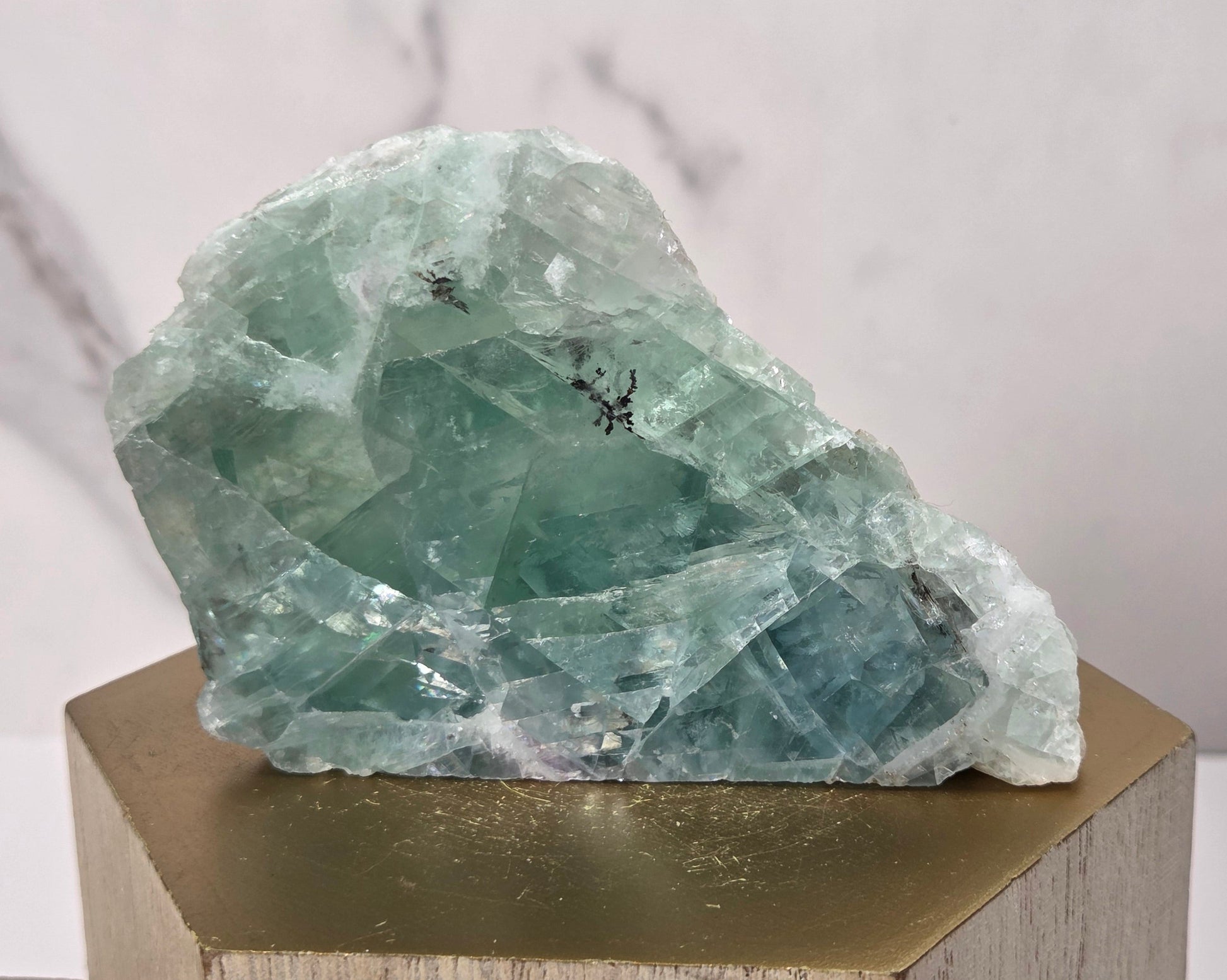 raw mineral and geode specimens displayed on wooden blocks against a white marble-patterned background. The stones feature natural patterns in shades of green, purple, blue, and gray.