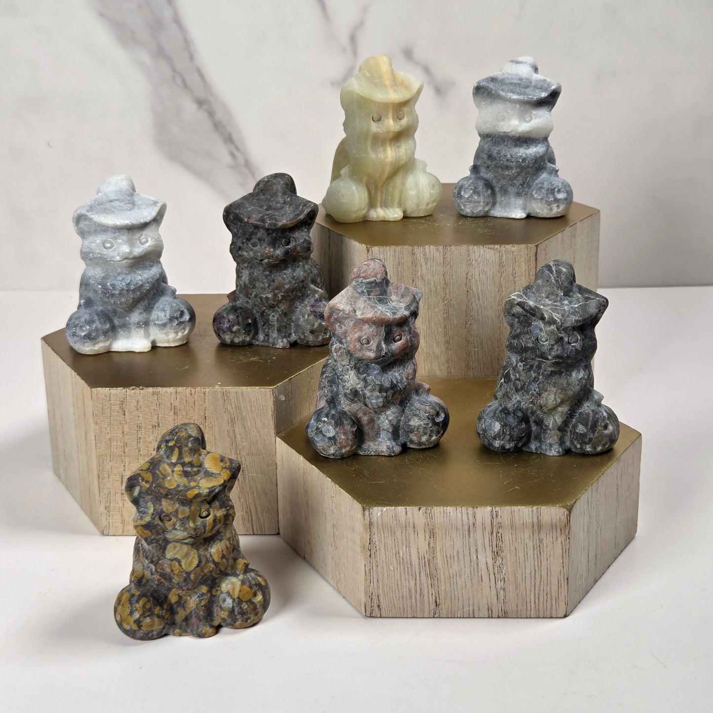 Six small stone lion figurines in various colors and patterns, arranged on a white surface with three hexagonal wooden pedestals against a light marble-patterned background.