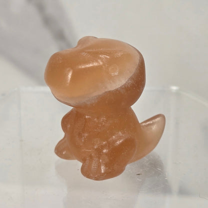 A small translucent peach-colored dinosaur figurine standing on a clear acrylic display base against a light marble-patterned background.
