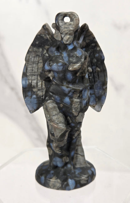 A small winged angel or cherub figurine made from mottled dark stone with blue and gray marbling, standing on a clear display base against a light marble-patterned background.