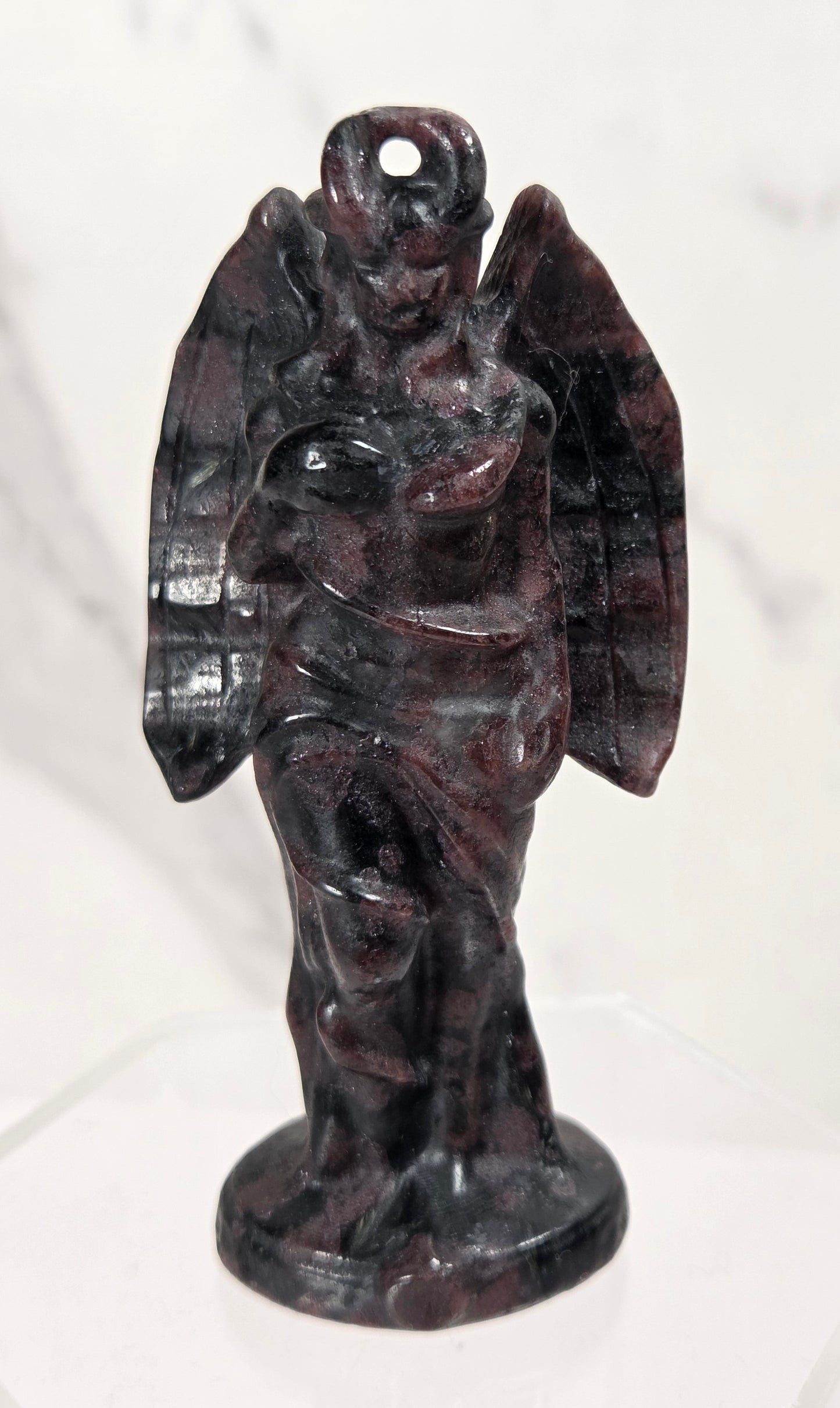 A small carved angel figurine made of dark polished stone, standing on a round base against a light marble-like background.