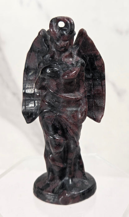 A small carved angel figurine made of dark polished stone, standing on a round base against a light marble-like background.
