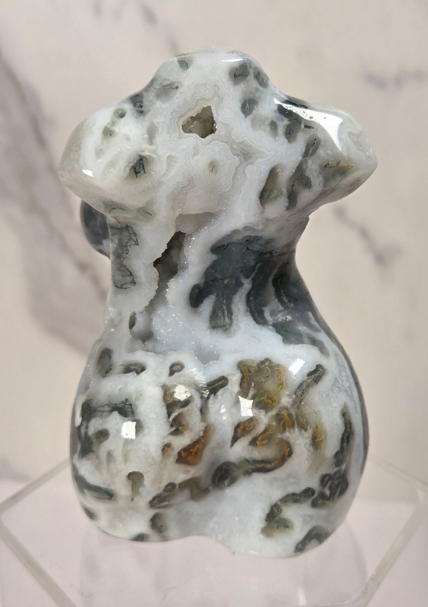 A polished carved stone figurine of a dog, featuring natural marbled patterns of white, gray, and brown, displayed on a clear acrylic stand against a light marble background.