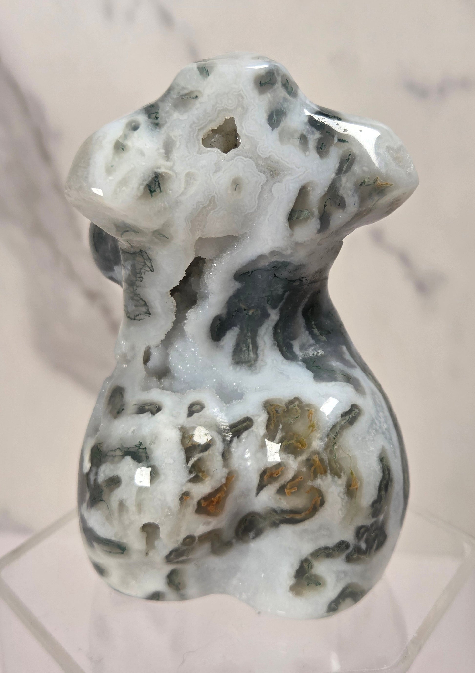 A polished carved stone figurine of a dog, featuring natural marbled patterns of white, gray, and brown, displayed on a clear acrylic stand against a light marble background.