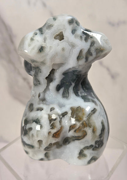 A polished carved stone figurine of a dog, featuring natural marbled patterns of white, gray, and brown, displayed on a clear acrylic stand against a light marble background.