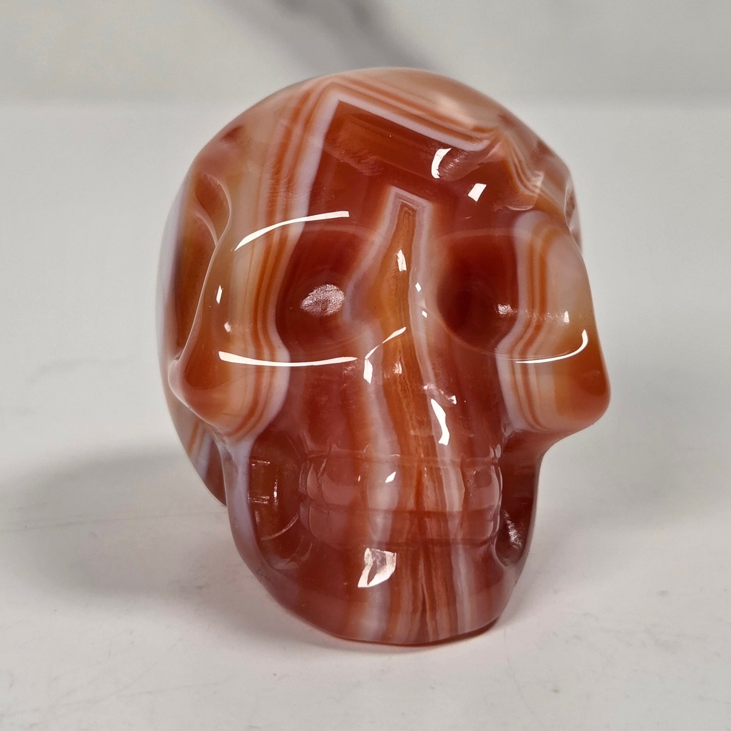 A polished carved skull made from red and white banded agate stone, displayed on a light gray surface.