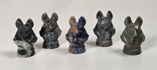 Five small carved stone animal figurines, including a mouse, rabbit, and fox, arranged in a row on a white surface with a light gray marble background.