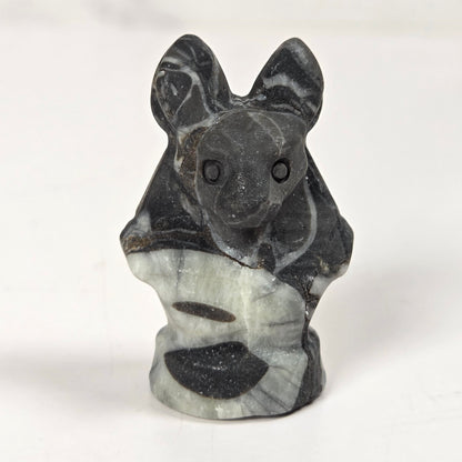 A small carved stone figurine of a bat or mouse, made from black and white marbled stone, standing upright on a light surface.