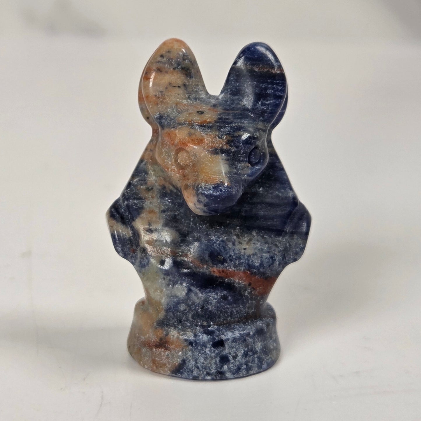 A small carved figurine of a rabbit made from polished blue and orange marbled stone, standing upright against a light gray and white marble background.