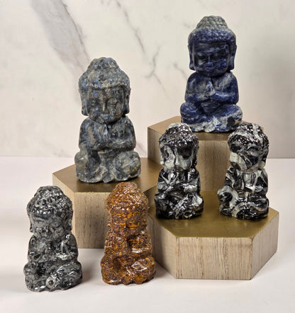 Buddha stone statues in various marbled colors are arranged on wooden display blocks against a light marble-patterned background.