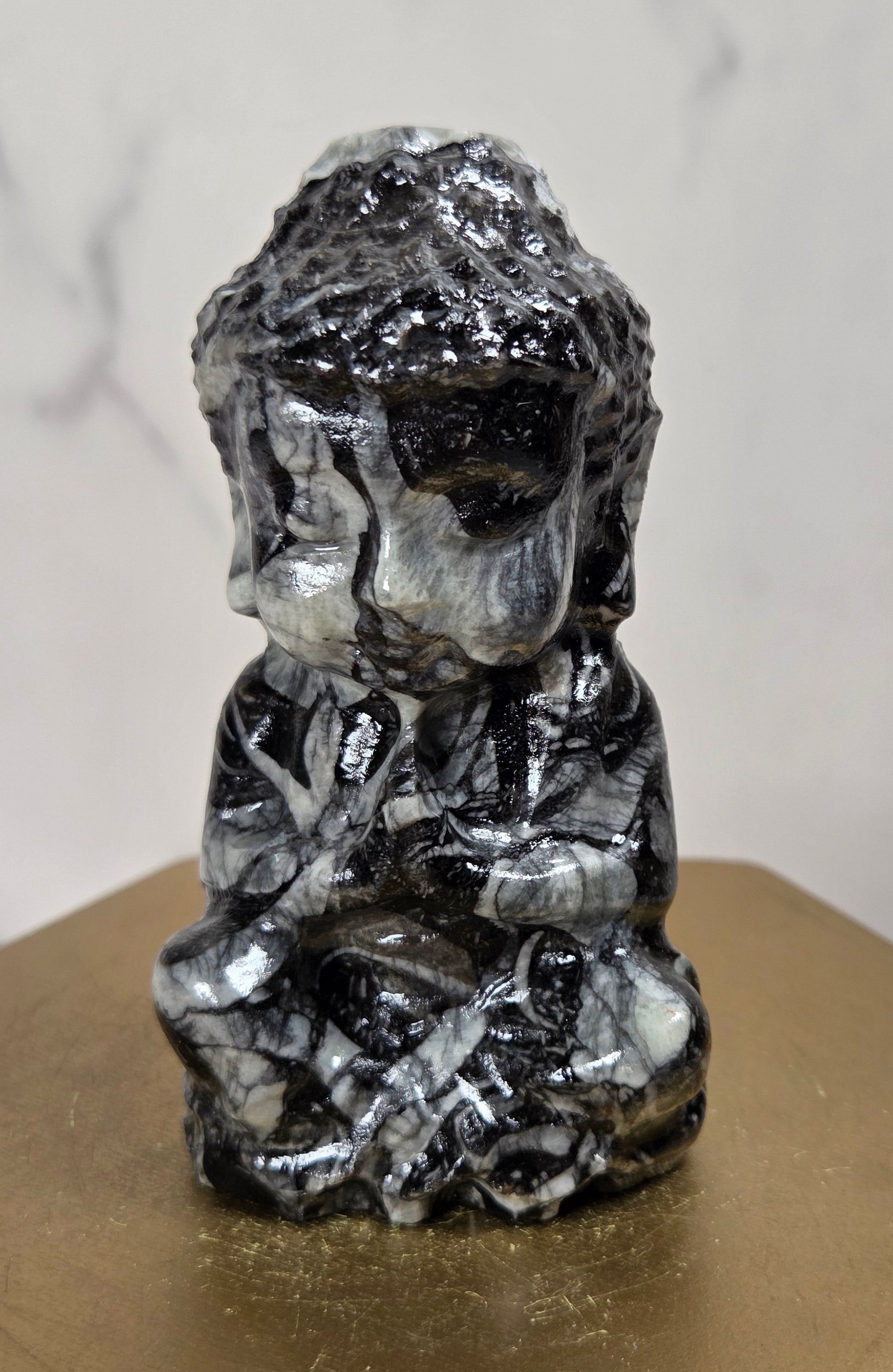 A small polished black and white marbled figurine of a seated person, displayed on a gold-colored hexagonal pedestal against a light marble-patterned background.