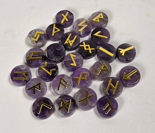 A pile of round purple amethyst cabochons, each engraved with a different gold rune symbol, arranged on a light gray textured surface.