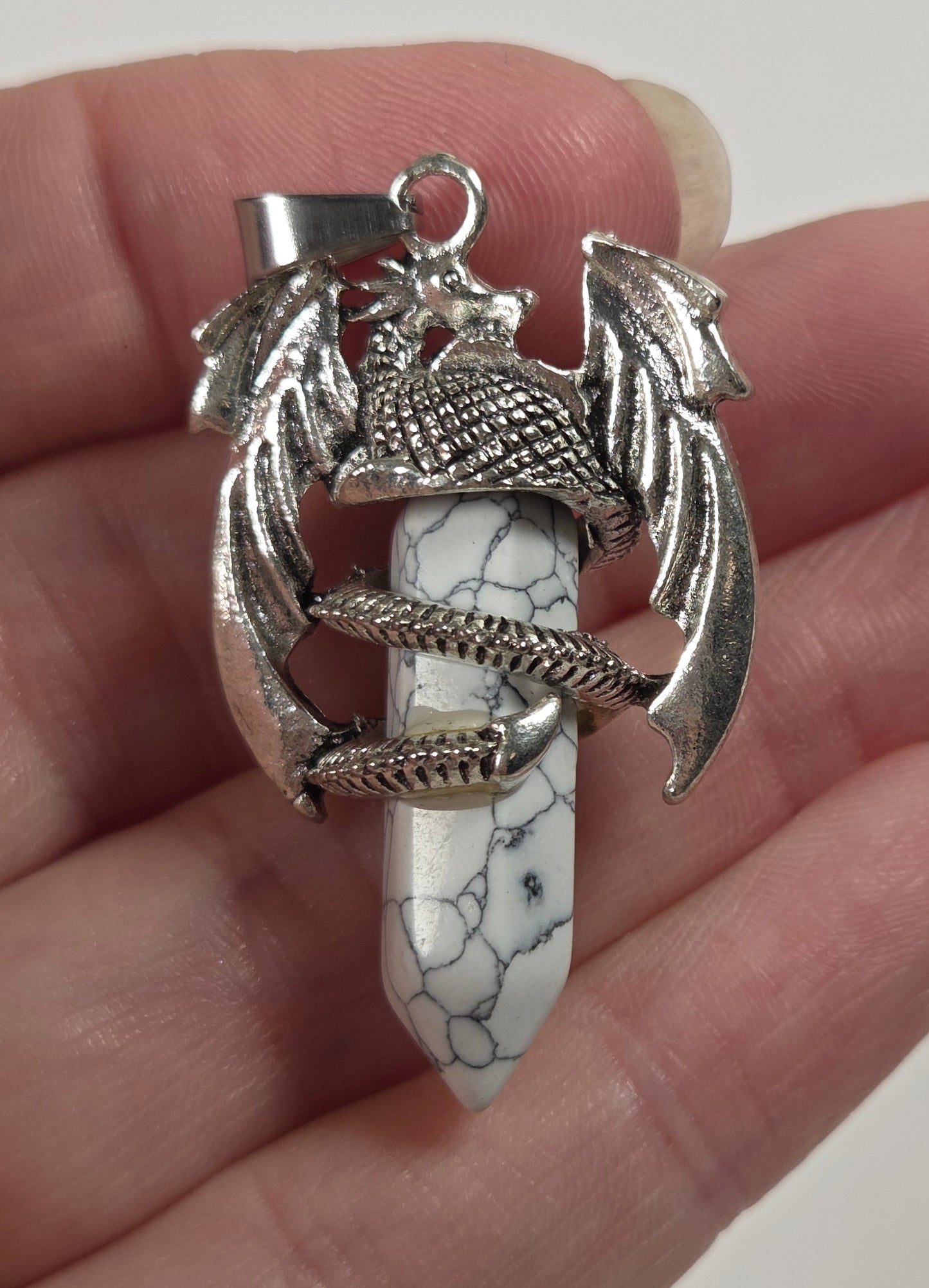 A hand holding a silver dragon pendant with a white and black marbled stone dagger hilt.