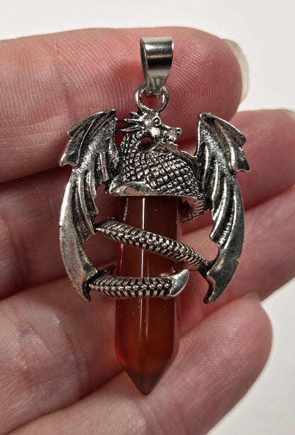 A hand holding a silver dragon pendant wrapped around a pointed amber-red gemstone, against a plain light background.