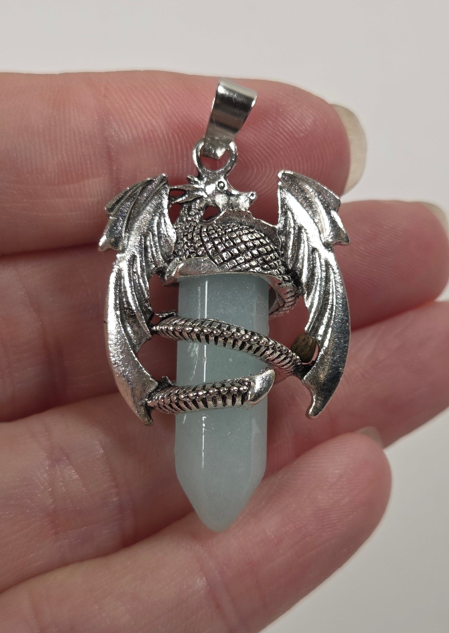 A silver dragon pendant holding a pale blue-green crystal point, held in a person's hand against a plain light background.