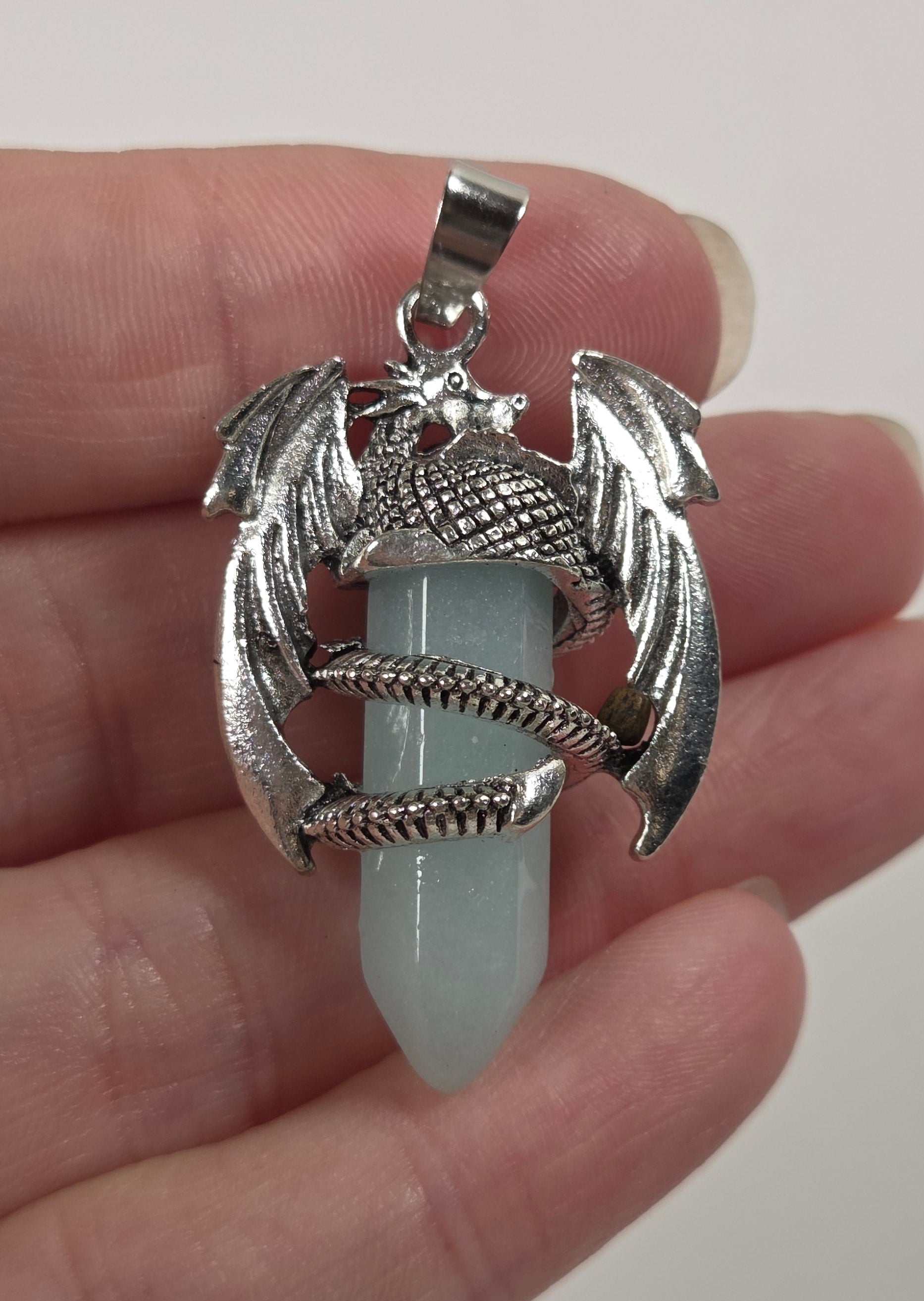 A silver dragon pendant holding a pale blue-green crystal point, held in a person's hand against a plain light background.