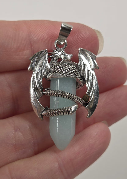 A silver dragon pendant holding a pale blue-green crystal point, held in a person's hand against a plain light background.