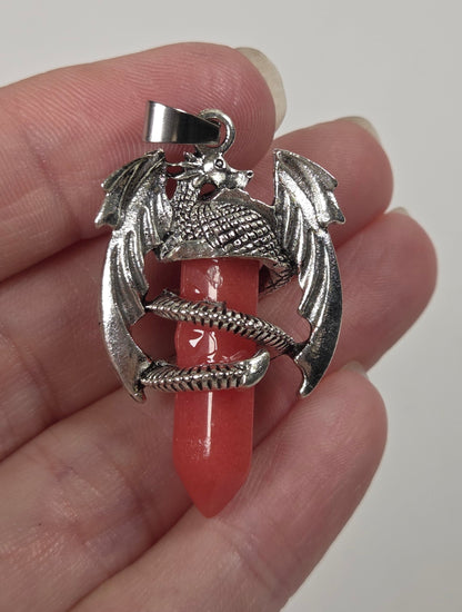 A hand holding a silver dragon pendant with a red coral or onyx core, against a plain light background.