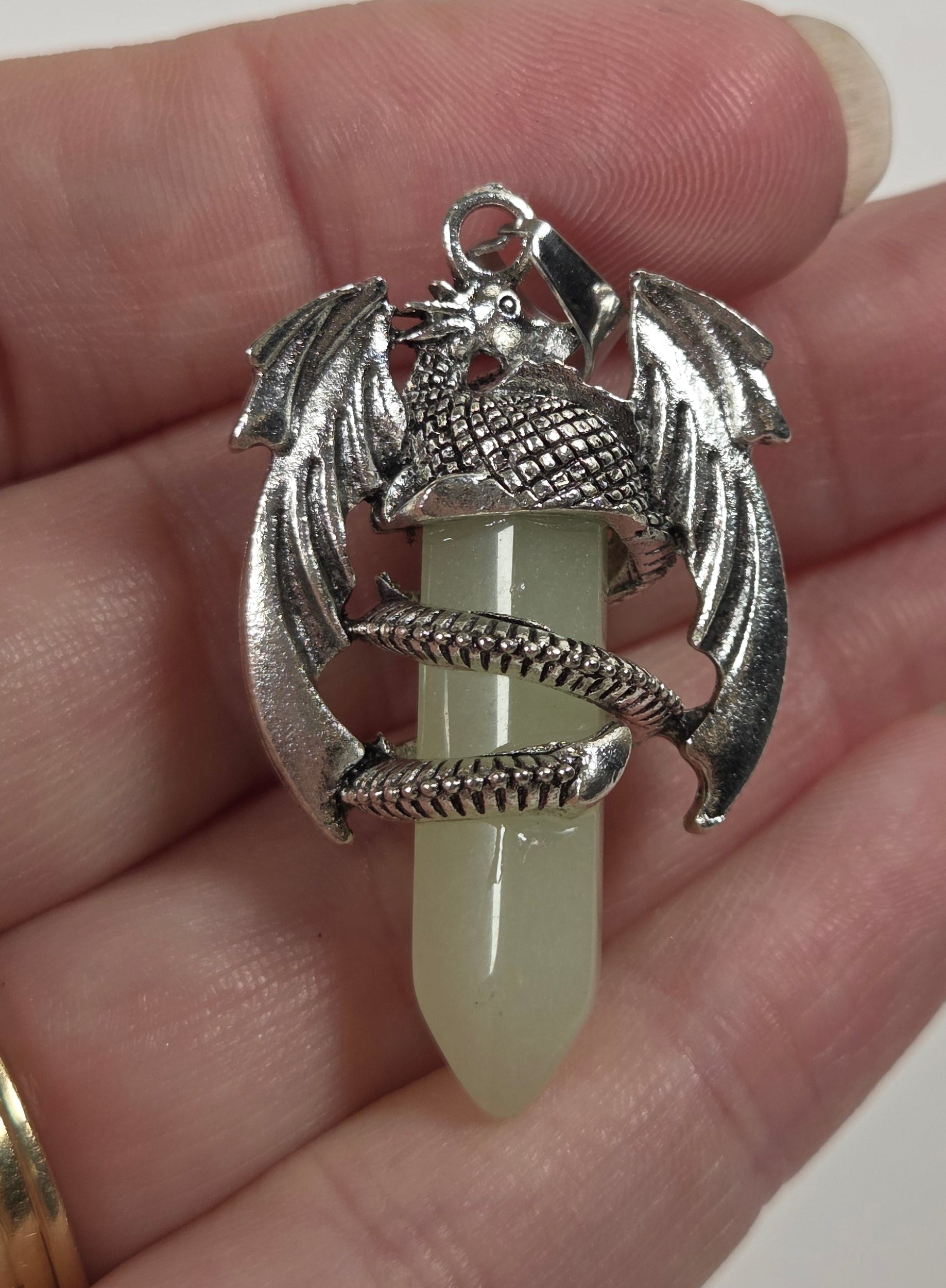 A hand holding a silver dragon pendant wrapped around a pale green jadeite point.