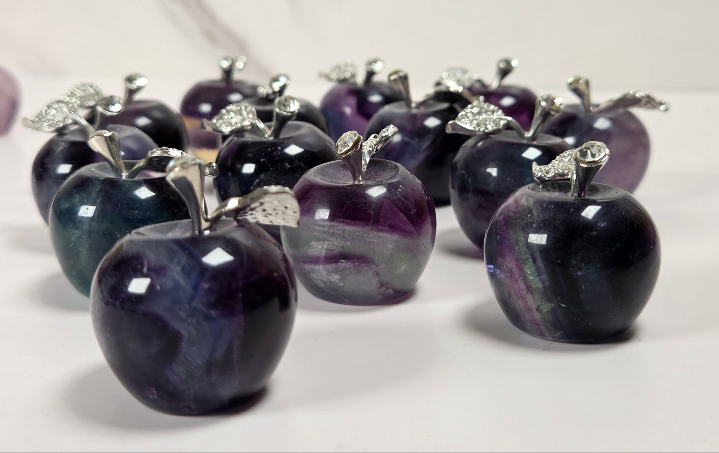 A group of polished dark purple and black stone apple figurines with silver-colored metal stems and leaves, arranged on a light surface.