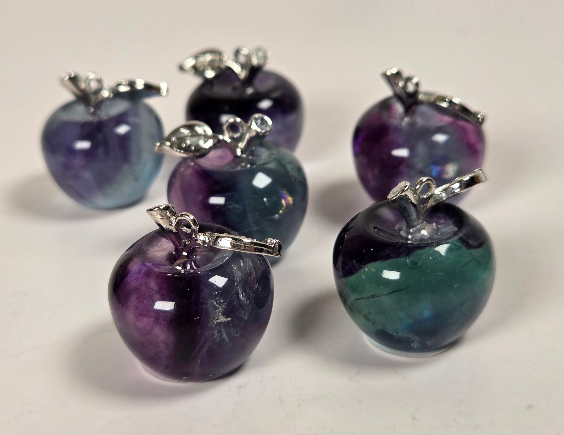 Five small glossy apple-shaped charms with silver-toned tops, shown on a plain light background. The apples have marbled colors including purple, blue, green, and dark tones.