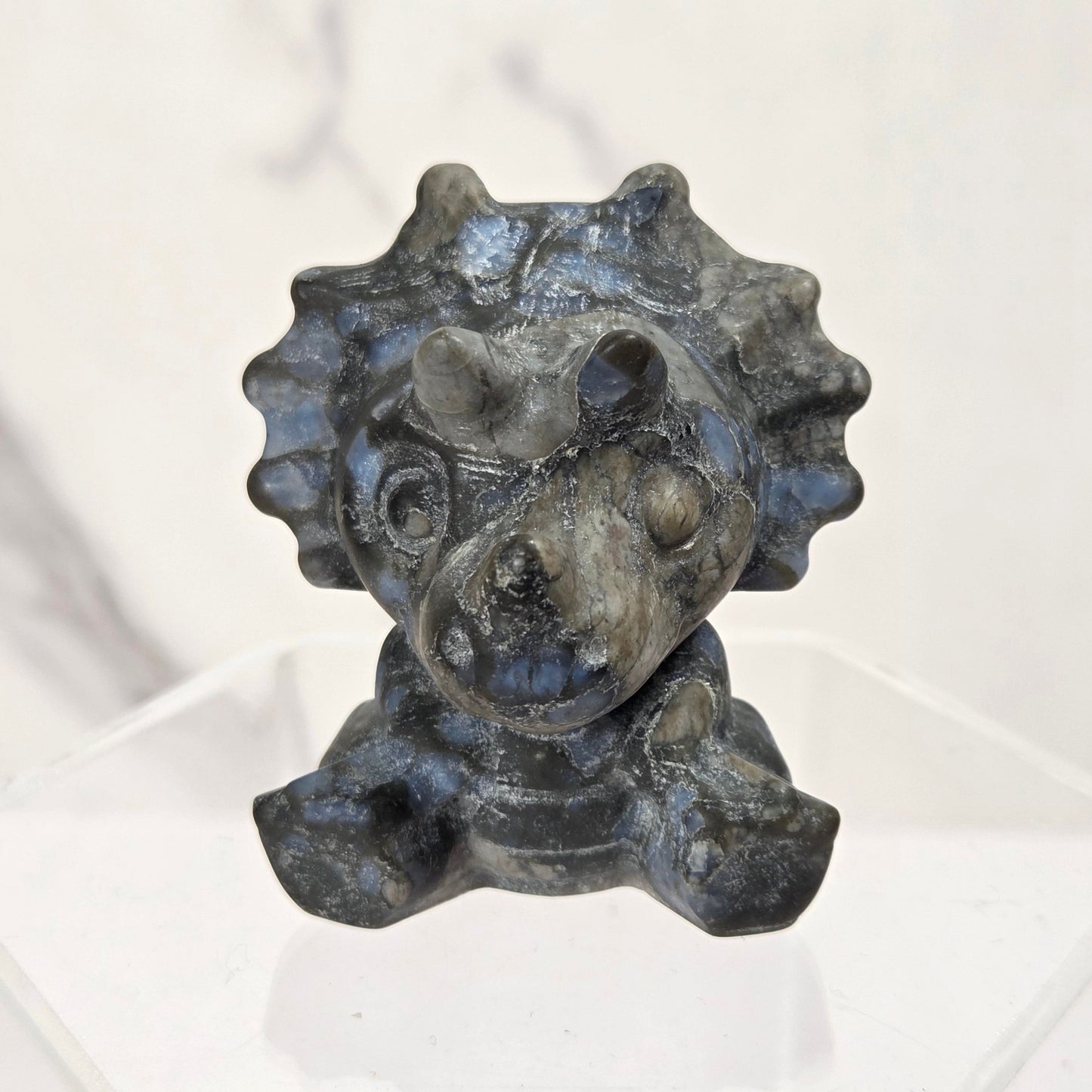 A small dark gray stone figurine of a cartoon character with a round head and spiky hair, displayed on a clear acrylic stand against a light marble-patterned background.