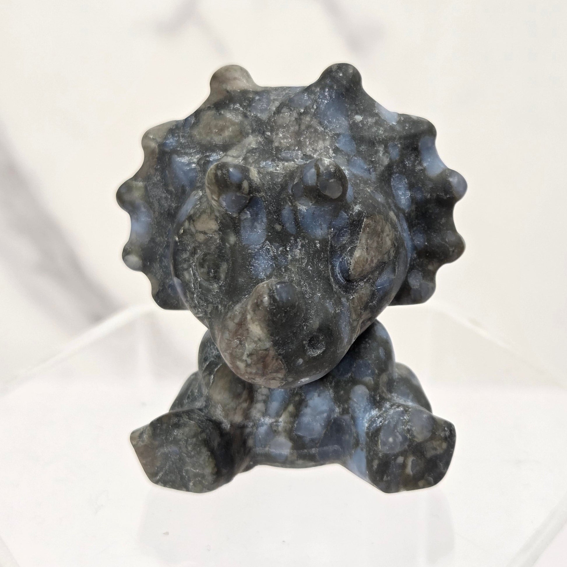 A small dark gray stone lion figurine with a textured, polished surface, displayed on a clear acrylic stand against a light gray marble-patterned background.