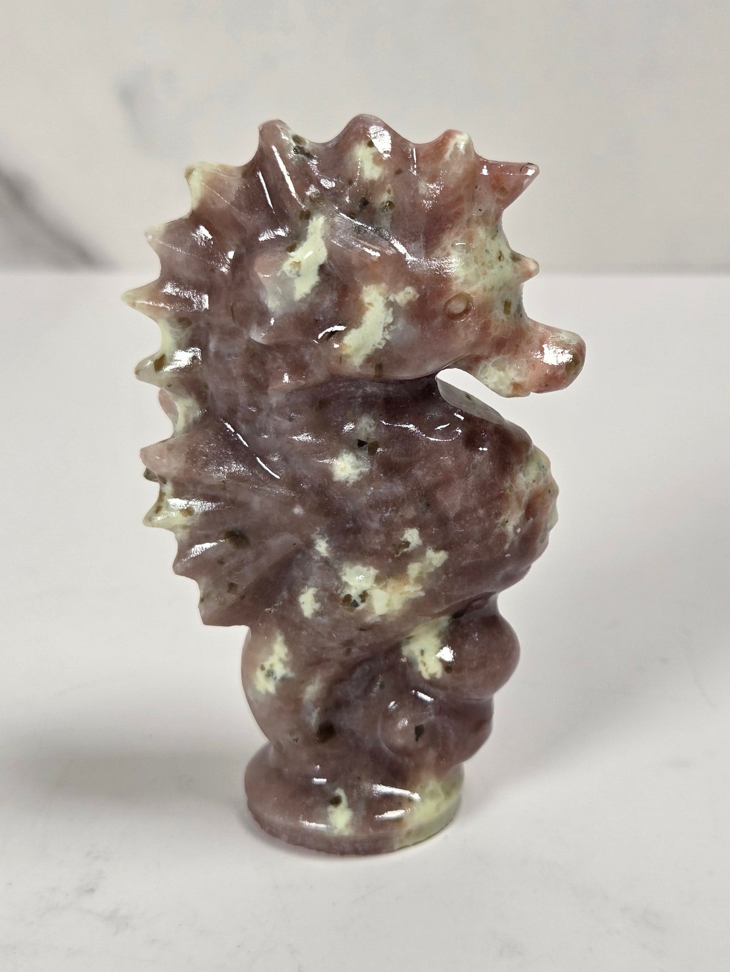A small carved seahorse figurine made from polished brown and cream stone, standing upright on a light gray marble-like surface.