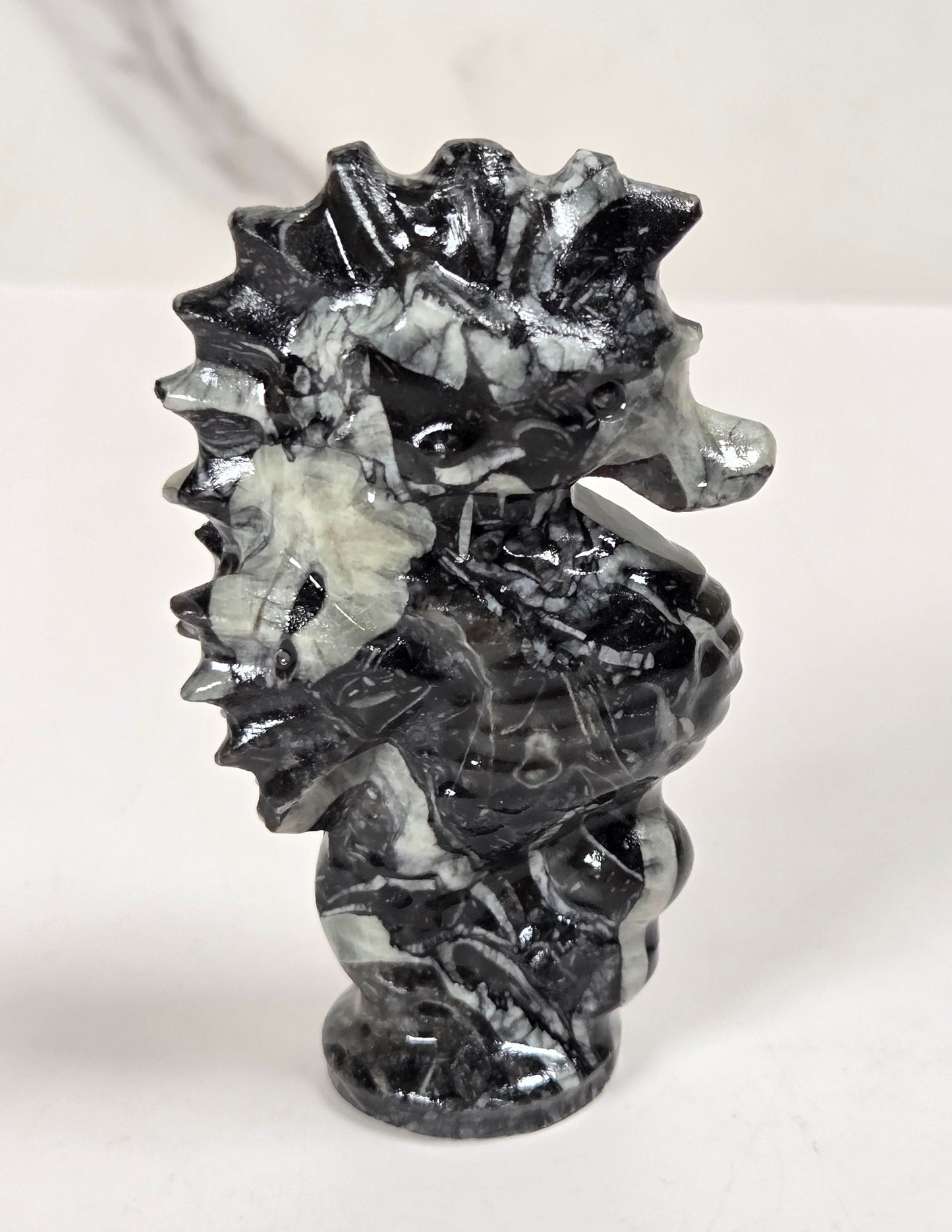 A small carved seahorse figurine made from black and white marbled stone, standing on a white surface against a light gray marble-patterned background.