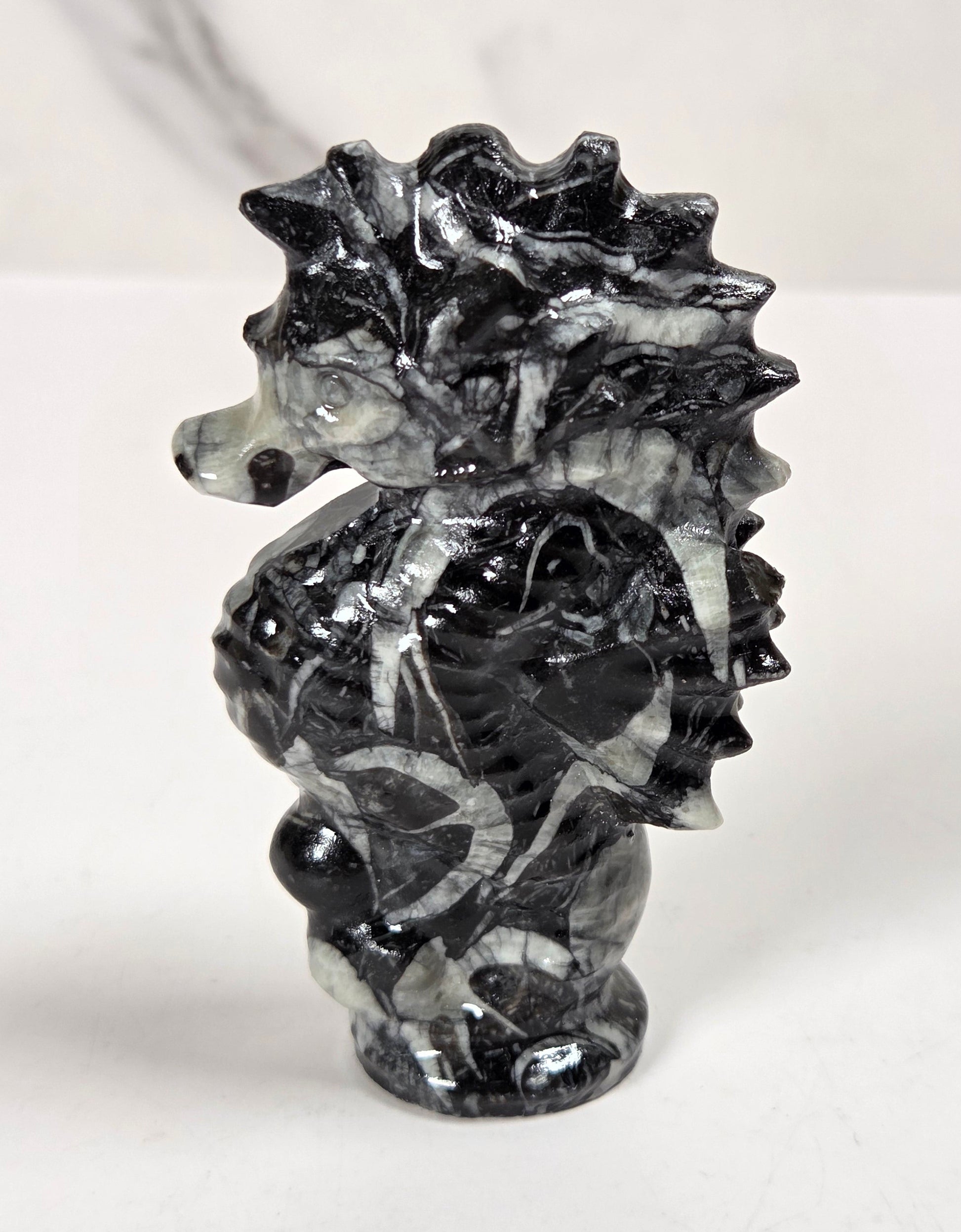 A small carved seahorse figurine made from black and white marbled stone, standing on a white surface against a light gray marble-patterned background.