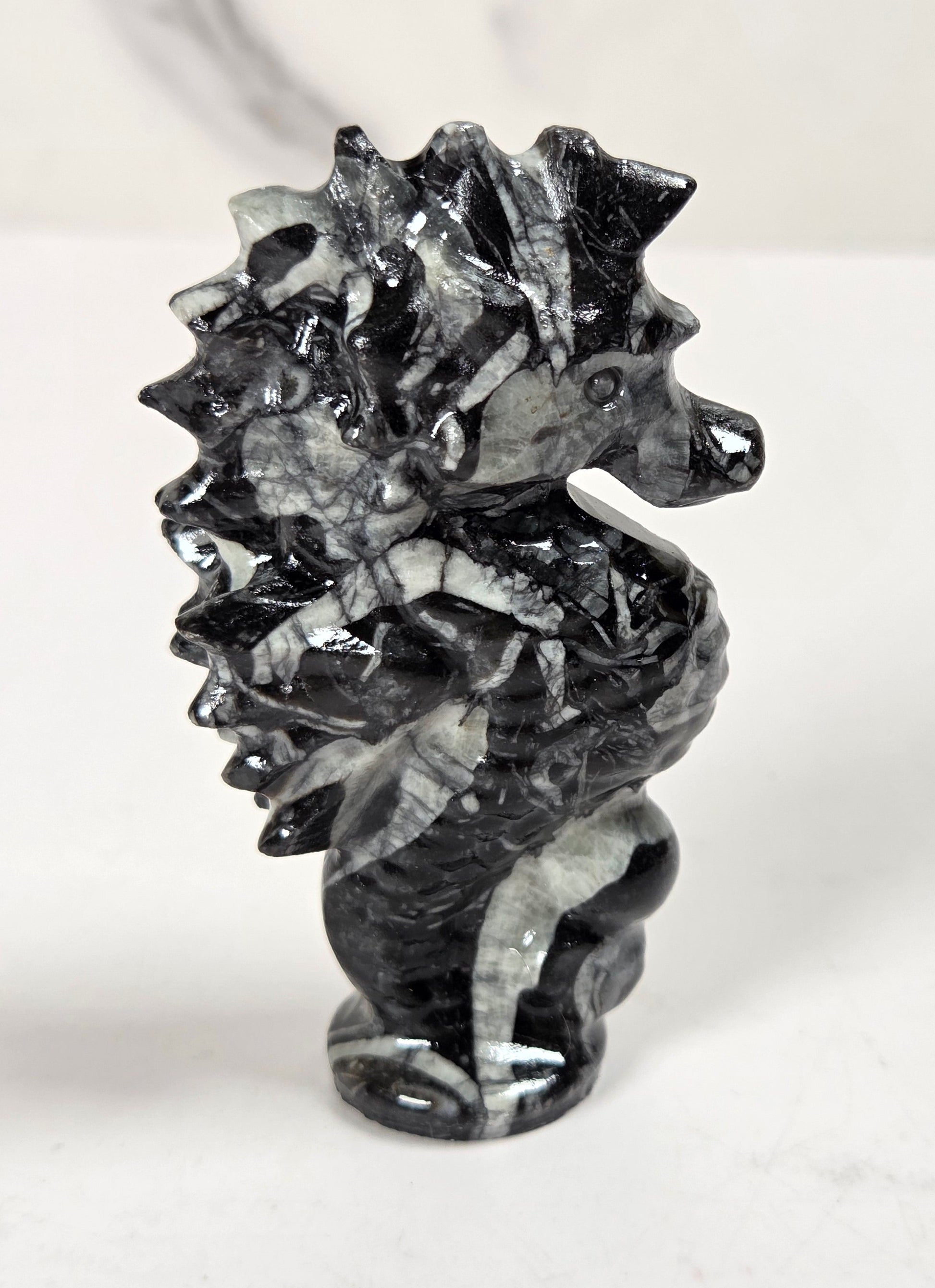A small carved seahorse figurine made from black and white marbled stone, standing on a light surface against a white background.
