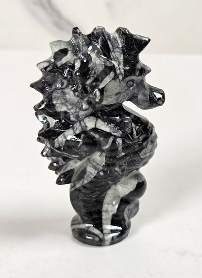 A small carved seahorse figurine made from black and white marbled stone, standing on a light surface against a white background.