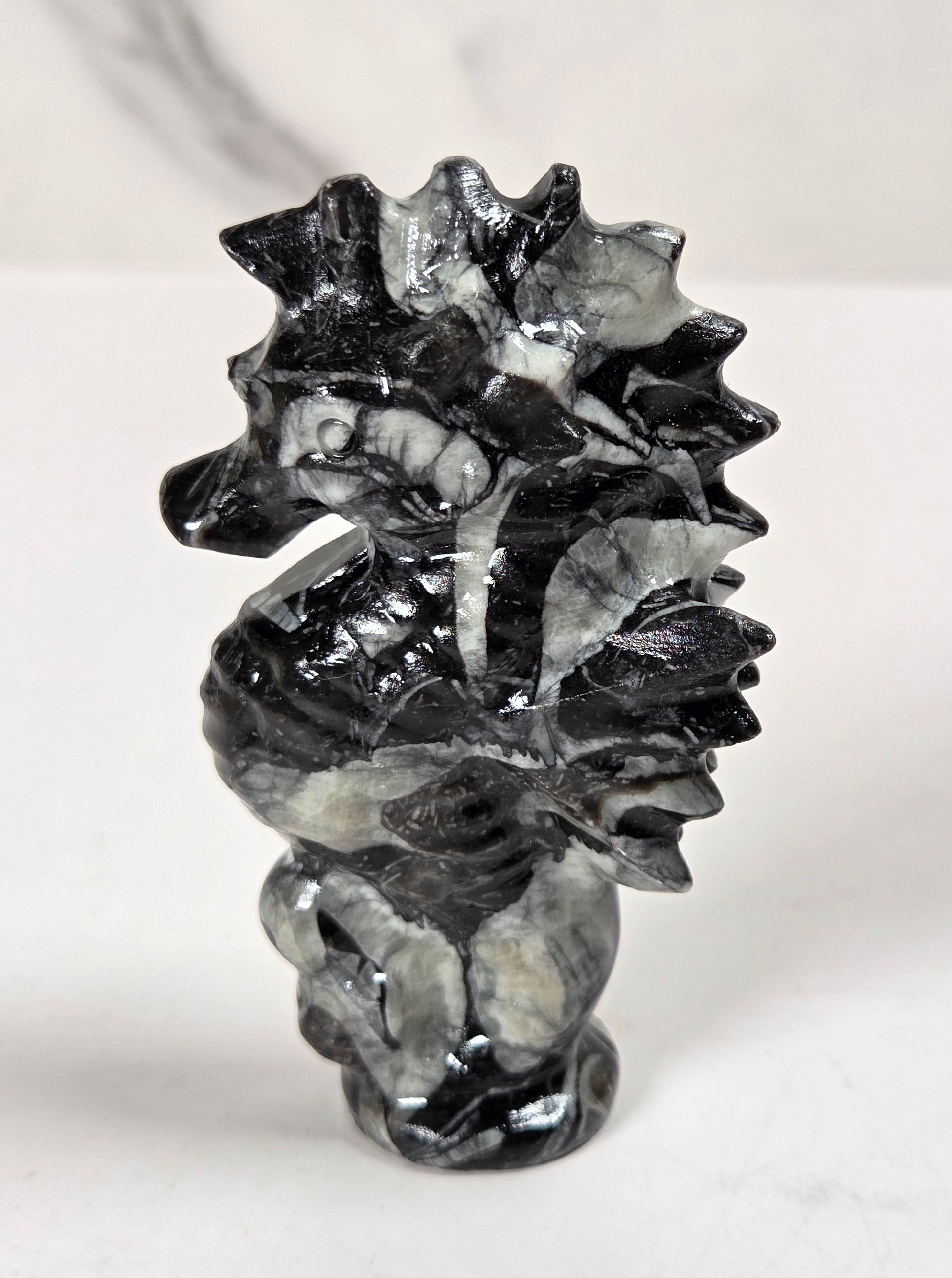 A polished black and gray seahorse figurine carved from a marbled stone, standing on a white surface against a light gray marble-patterned background.