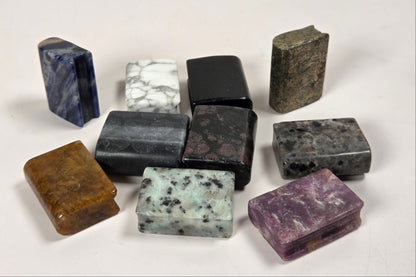 A group of nine polished rectangular gemstone blocks in various colors and patterns, arranged on a plain off-white background.